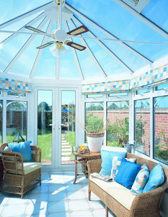 Victorian conservatory interior with blue-tinted roof panels, wicker seating, ceiling fan and garden doors.
