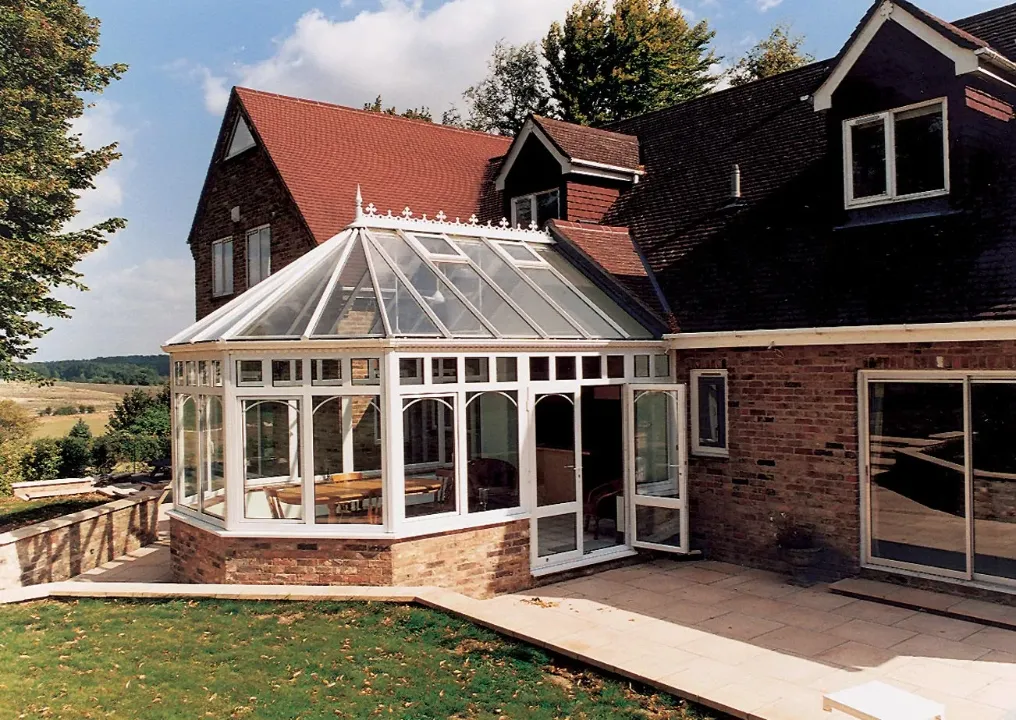 Large white Victorian conservatory with arched glazing, glass roof, brick base and open patio door.