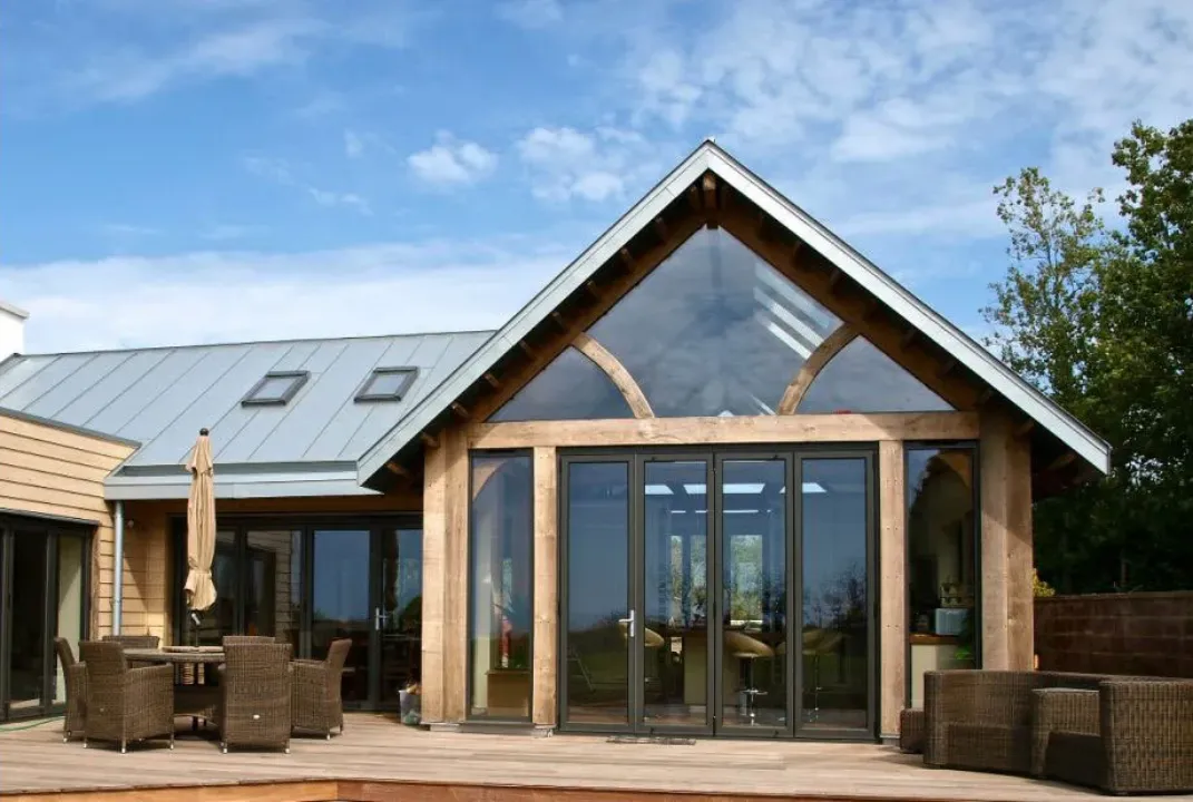 Black aluminium bifold doors beneath a glazed gable on an oak-framed extension