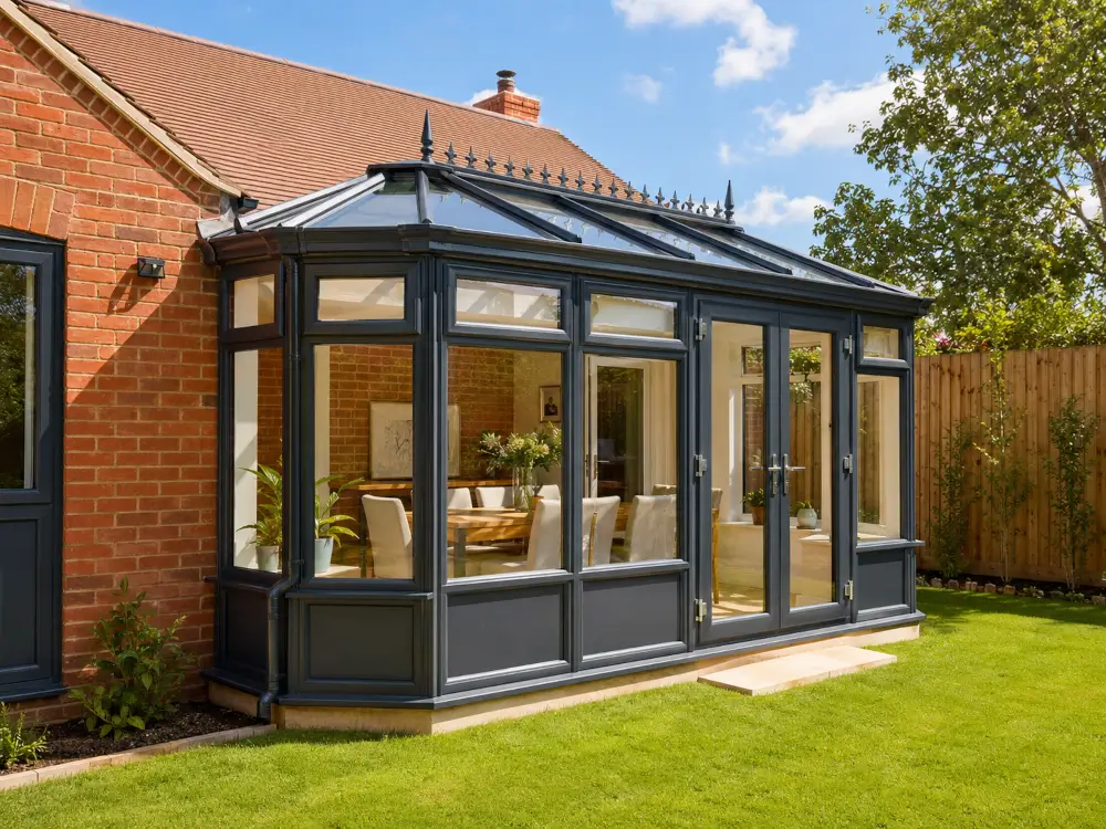 Conservatory {location} with anthracite frames, decorative glazed roof, French doors and a bright dining area attached to a brick home.