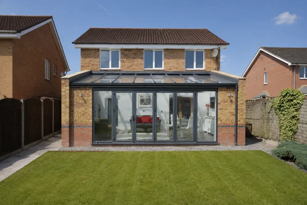Conservatory {location} with lean-to glazed roof, dark frames, wide doors and a bright living room opening onto a garden.