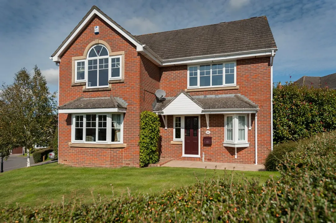 Red brick house with white uPVC casement windows, bay window and arched feature window above the lawn.